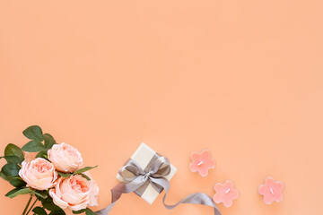 Spring composition with flowers and gift box with ribbon on pastel peach background. Greeting card for spring holiday Birthday, Woman or Mothers Day.