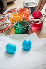 Frau holt fertig gefärbte bunte Ostereier Eier mit Löffel aus Kaltfarben in Rot, Orange, Gelb, Blau, Grün in Glas auf Papiertuch zum Abtropfen zu Ostern