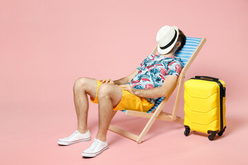 Full length of young traveler tourist man in summer clothes sit on deck chair covering face with...