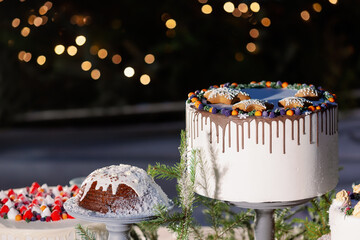 Wedding white beautiful cake decorated with cherries, raspberries, strawberries on cake stand with fir tree, cookies and xmas decoration on wood table. Blurred background