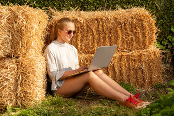Fille blonde adossée à une botte de foin travaillant sur son ordinateur portable