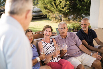 gruppo di famiglia si rilassa divertito in giardino brindando con un aperitivo seduti in un divano...