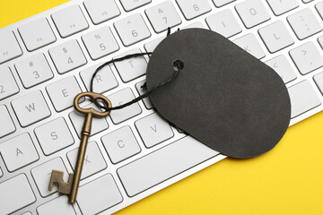 Vintage key with blank tag and keyboard on yellow background, closeup. Keyword concept