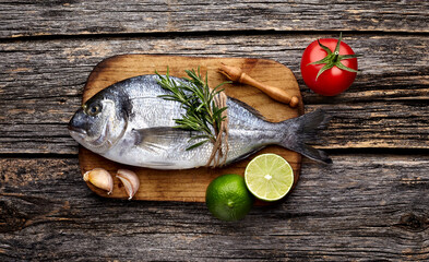 Dorado fish on the wooden  with lime, rosemary, garlic  and tomato. Top view.