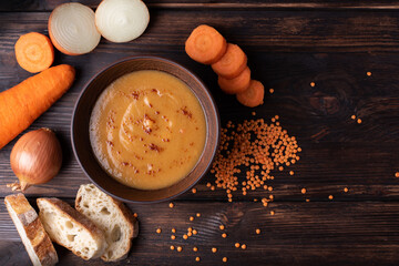 Hot red lentil cream soup with ingredients on a wooden table