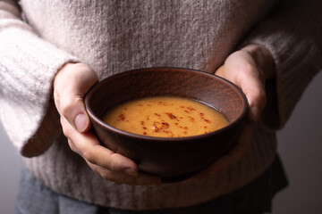 Female hands holding a bowl of vegetarian red lentil cream soup.