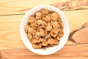 Natural multi-grain flakes in a white saucer on a wooden table, close-up, top view.