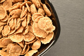 Natural multi-grain flakes in a black ceramic plate on a slate board, close-up, top view.