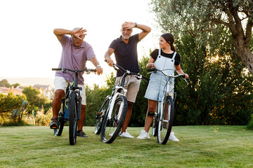 Tre persone di generazioni diverse si divertono ad andare in bicicletta in un prato verde - obrazy, fototapety, plakaty