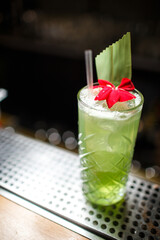 green tropical cocktail with red flower decoration on steel bar on dark background close up