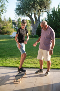 Nipote adolescente insegna in giardino al nonno Anziano ad andare sullo skateboard 