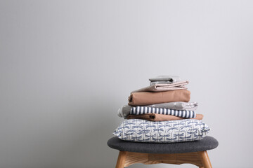 Stack of clean bed linen and pillow on stool near light grey wall. Space for text