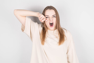 Young woman with disheveled hair yawns from fatigue against gray wall