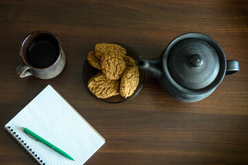 The table on which there is a mug of tea biscuits, a notebook, a pen.