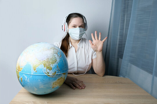 girl with long hair wearing headphones, medical mask leading conference, shows place on the globe from home office, concept of remote education, video conference, foreign language lesson