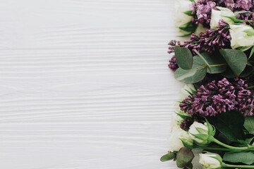 Floral border composition, lilac and roses flat lay on white wood with space for text