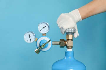 Medical worker checking oxygen tank on light blue background, closeup
