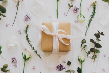 Stylish gift box with lilac and roses flowers and eucalyptus, flat lay on white wood. Mothers day