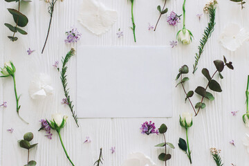 White paper card and lilac, roses and eucalyptus  flowers composition on white wood flat lay