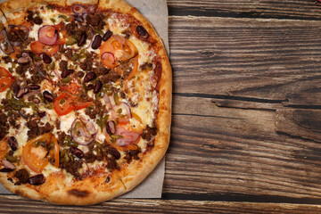 Top view of fresh baked pizza with meat and vegetables on a wooden table. Pizza delivery. Take away.	

