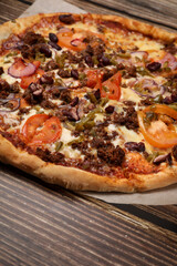 Top view of fresh baked pizza with meat and vegetables on a wooden table. Pizza delivery. Take away.	
