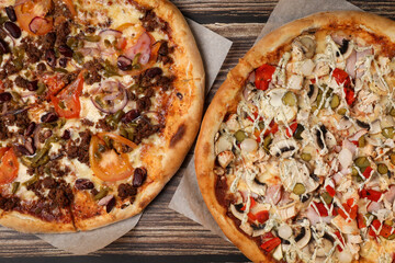 Top view of 2 fresh baked pizza with meat , mushrooms and vegetables on a wooden table. Pizza delivery. Take away.	