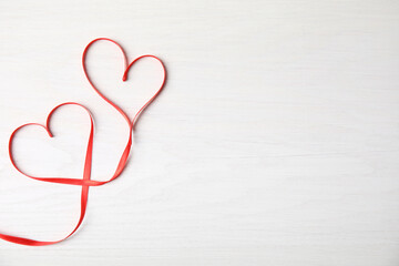 Hearts made of red ribbon on white wooden background, top view with space for text. Valentine's day celebration