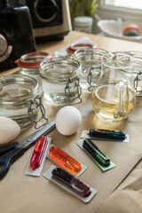 Bunte Ostereier Kaltfarben in Rot, Orange, Gelb, Blau, Grün in Verpackung auf Papier Unterlage mit Eier, Essig, Wasser, Gläser und Schere zum Färben zu Ostern