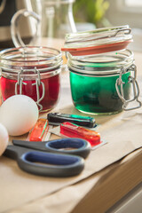 Bunte Ostereier Kaltfarben in Rot, Orange, Gelb, Blau, Grün in Verpackung auf Papier Unterlage mit Eier, Essig, Wasser, Gläser und Schere zum Färben zu Ostern
