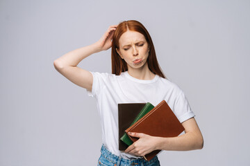 Displeased sad young woman college student holding book and looking at camera on gray isolated background. Pretty redhead lady model wearing casual clothes emotionally showing facial expressions.