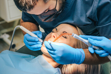 The girl at the reception of a male dentist in a dental chair, with her mouth open during the procedure, closed her eyes in fear.