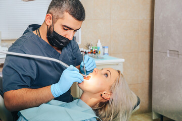 Obraz na płótnie Canvas A girl at the reception of a male dentist in a dental chair, with her mouth open during the procedure.