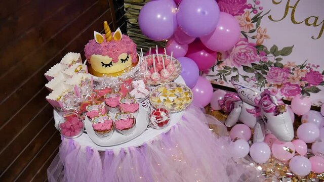 Sweet unicorn style table for Birthday. Cake, muffins, marshmallows, sucking candy, cheese and hard candy. Inflatable unicorn balloon