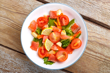 Salad with salmon and cherry tomatoes and green salad in a plate on a wooden table. Copy space.