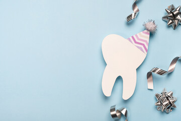 Decorative model tooth in a festive cap on light blue background. Dentist day, birthday or sale....