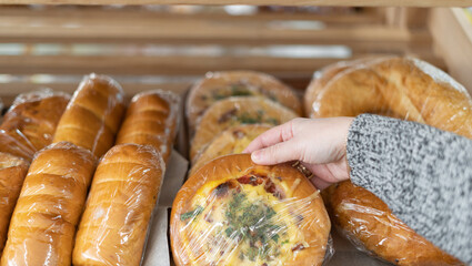 A woman's hand takes a small white flour pizza from a wooden shelf in a supermarket. Department of flour products.