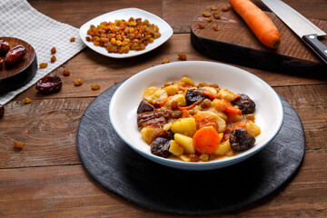 Jewish cuisine dish sweet tsimes with carrot dates vegetarian in a clay plate on a wooden board near candied fruits.