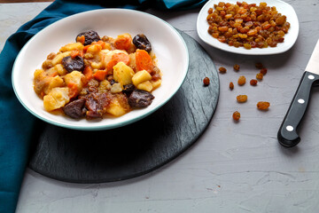 A dish of Jewish cuisine sweet tsimes with carrots vegetarian dates in a plate on a round stand on a concrete background next to raisins on a saucer.