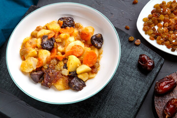 Jewish cuisine dish sweet zimmes with vegetarian dates carrots in a plate on a concrete background on a black board.