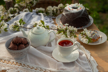 Tea set on a white tablecloth on a sunny day, cherry blossom branches, marshmallows in chocolate, pudding, cupcake, wooden table. Outdoor breakfast, picnic, brunch, spring mood. Soft focus