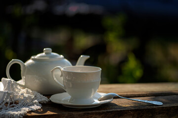 Elegant cup, lace tablecloth, teapot, wooden table. Outdoor breakfast, picnic, brunch, spring mood. Soft focus