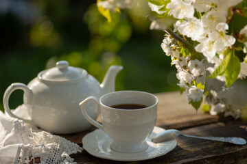 Elegant cup, lace tablecloth, teapot, wooden table. Outdoor breakfast, picnic, brunch, spring mood. Soft focus