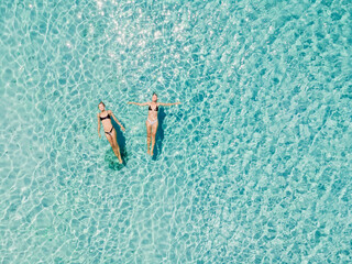 Couple of woman floating in clear blue sea. Aerial view