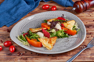Salad with grilled cheese and persimmon, wooden background