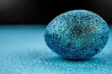 Trendy easter background with shiny blue colored egg and with glitters around. Creative spring holiday image with painted chicken egg. Top view flat lay still life. Easter concept.