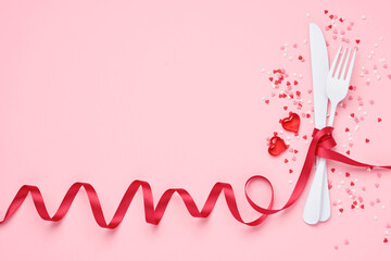 Valentines day background or concept for lunch menu. Cutlery white fork and knife entwined with red ribbon and small hearts on pink background. Top view.