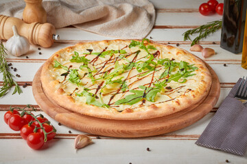 Pizza with slices, sauce and herbs, wooden white background