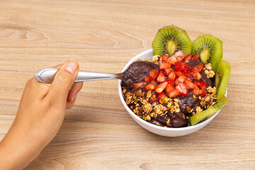 Hand picking up a spoon from the bowl of açai ice cream.