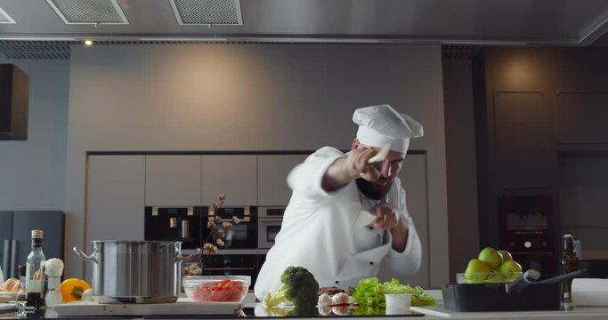Man chef having fun and doing karate with kitchen utensils looking at camera