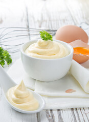 Bowl of Mayonnaise sauce on white wooden table, close-up